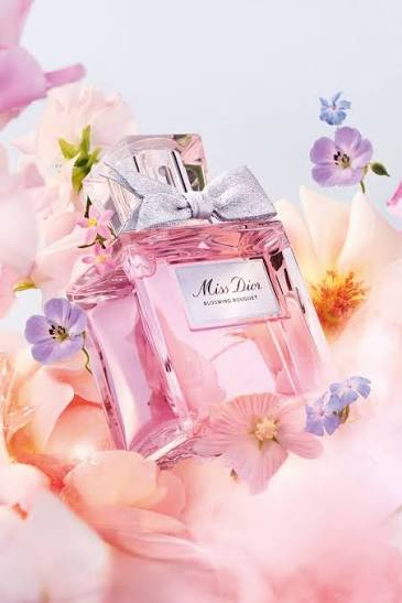 Pink Dior perfume bottle surrounded by flowers on a soft pink background