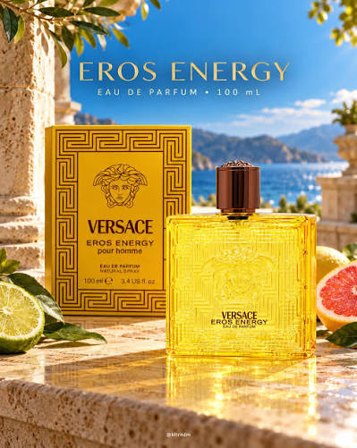 Versace Eros Energy Eau de Parfum 100 ml bottle and its gold box, styled on a stone ledge with citrus slices and a scenic Mediterranean background.