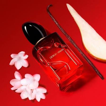 Perfume bottle with black cap and clear body on a red background with flowers and a pear slice.