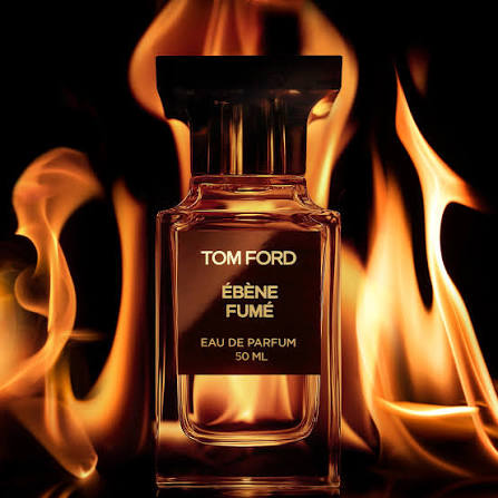 A Tom Ford Eau de Parfum bottle labeled “Ébène Fumé 50 ML” stands centered against a dramatic black background with glowing orange and yellow flames around it.