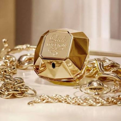 Gold perfume bottle with 'Ladur Million' text, surrounded by gold chains on a light background