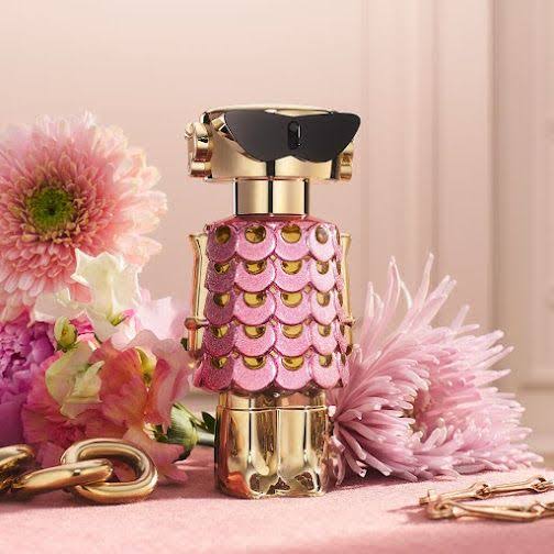 Perfume bottle with pink and gold design surrounded by flowers on a pink background