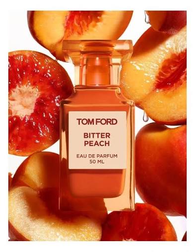 A 50 ml bottle of Tom Ford Bitter Peach Eau de Parfum, featuring a warm peach-colored liquid in a clear glass bottle with a cream label, surrounded by fresh peach slices on a white background.