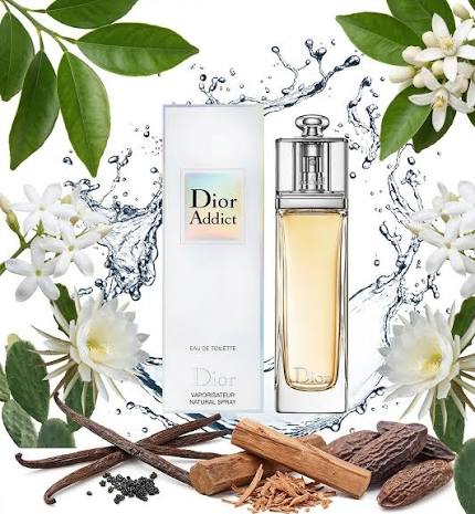Dior Addict Eau de Toilette bottle and box shown with white flowers, green leaves, vanilla beans, and cinnamon sticks on a white background with water splash graphics.